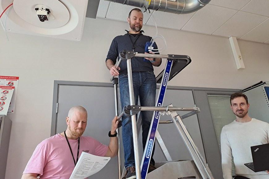 Kolme miestä ilmanvaihtolaboratoriossa tekemässä mittauksia.