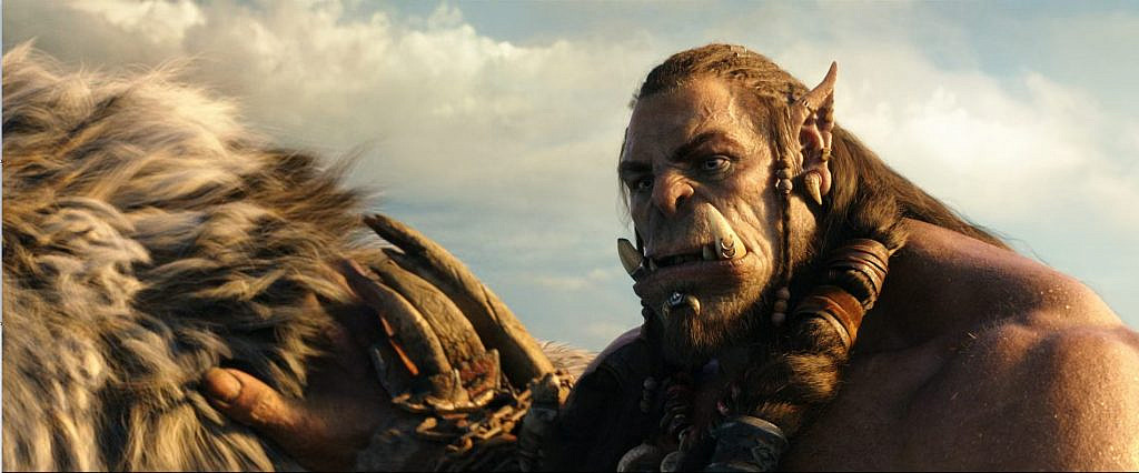 A brown orc, sporting two large fangs, a pointy ear and braids.