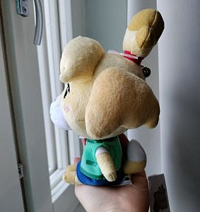 Plushie of Isabelle the dog sitting on a person's hand, facing left.