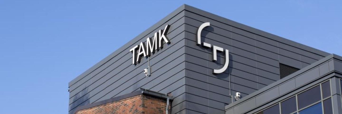 Rakennus, jonka seinässä TAMKin logo. Taustalla sininen taivas. 