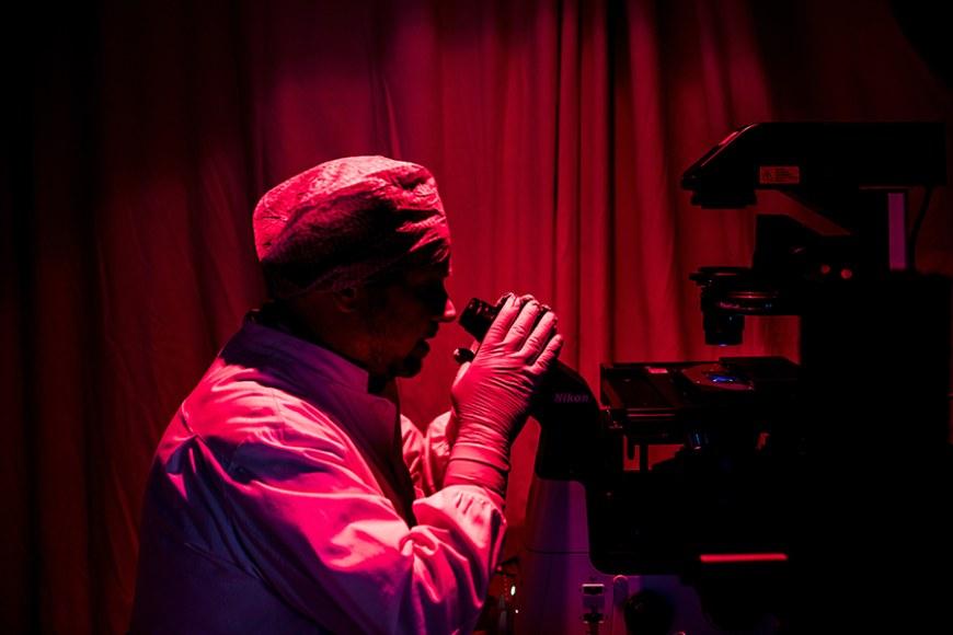 viitekuvassa suojavarusteissa oleva mies katsoo mikroskooppiin