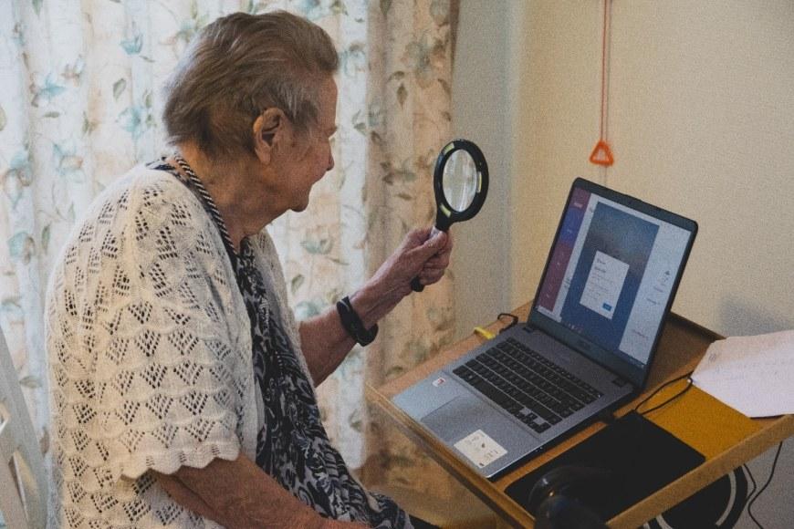An older adult is looking at a computer screen through a magnifying glass