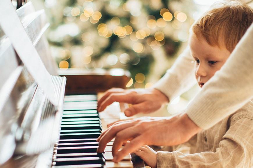 Lapsi ja aikuinen soittavat pianoa, taustalla joulukuusi.