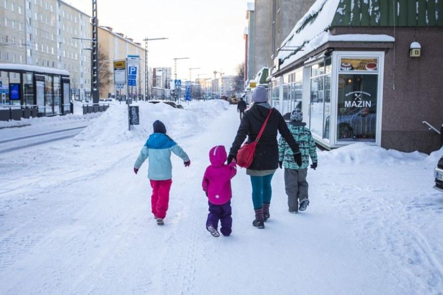 Aikuinen ja kolme lasta kävelevät kaupungilla talvella.