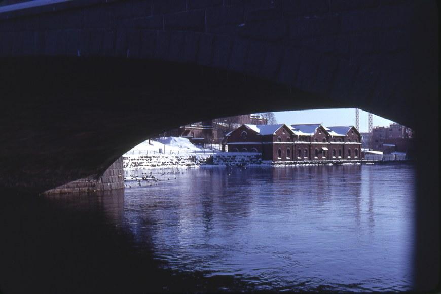 Näkymä Tammerkoskella sillan aukosta, vettä, taustalla punatiilinen rakennus.
