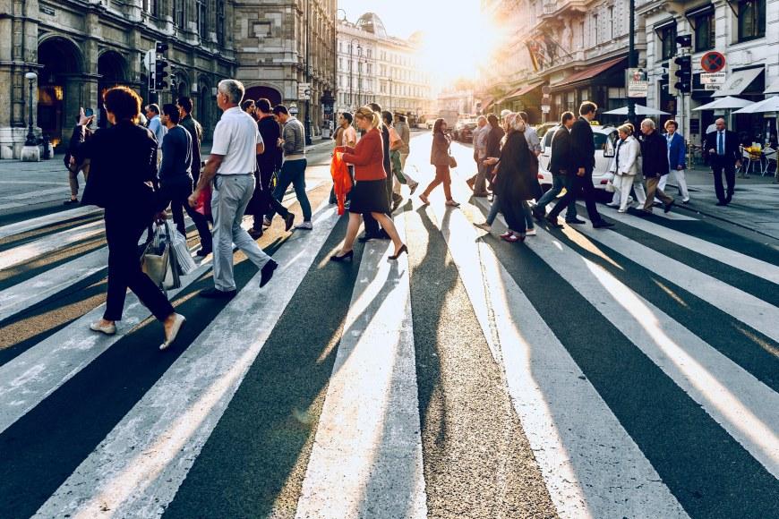 People crossing a road on a crosswalk. The sun is shining behind them.