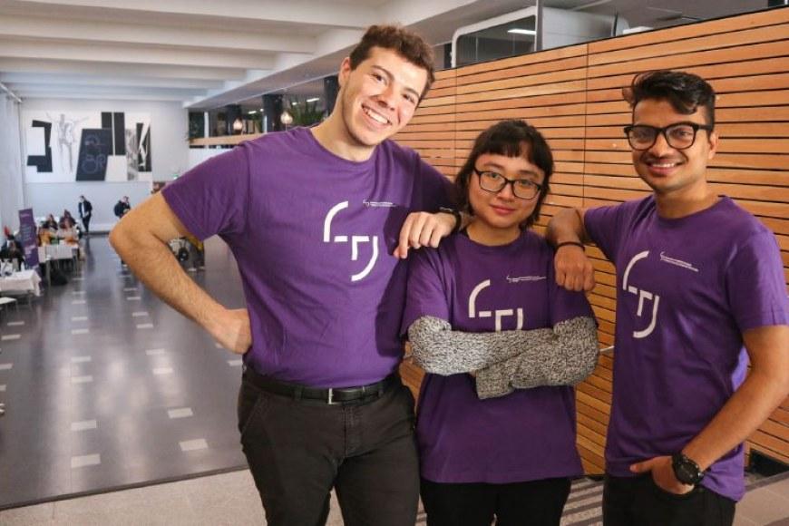 Opiskelijalähettiläitä kuvattuna TAMKin ruokalan ja juhlasalin edustalla violeteissa paidoissa, joissa korkeakouluyhteisön logo.