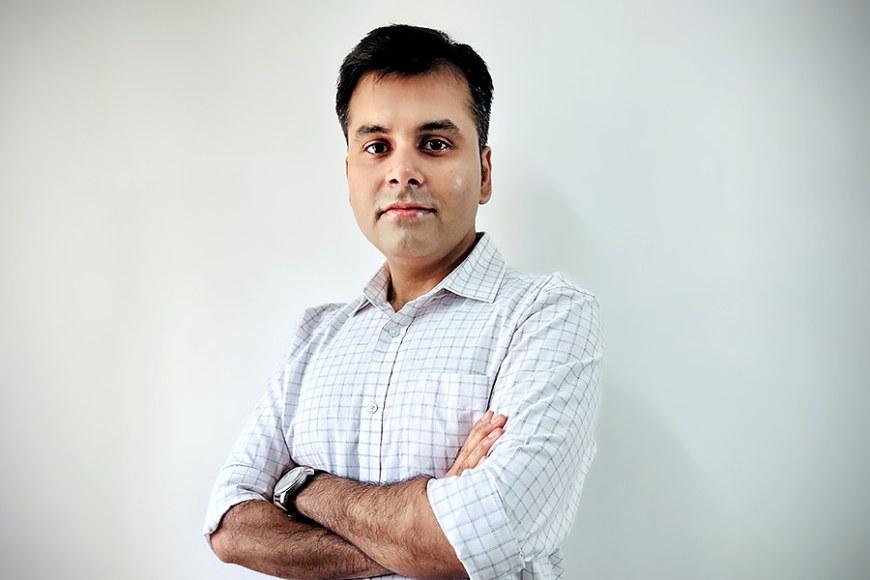 Bireshwar Sinha stands with his arms crossed in front of a pale wall. He is wearing a light collared shirt.