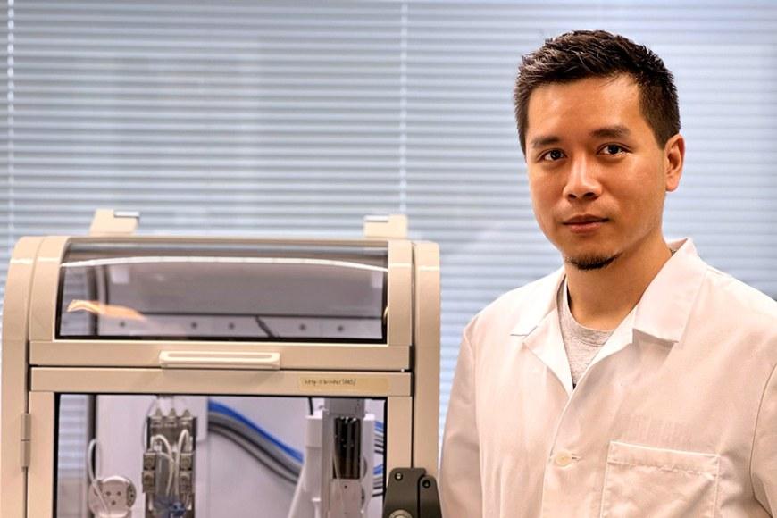 Hatai Jongprasitkul seisoo valkoinen takki yllään 3D-tulostimen vieressä.