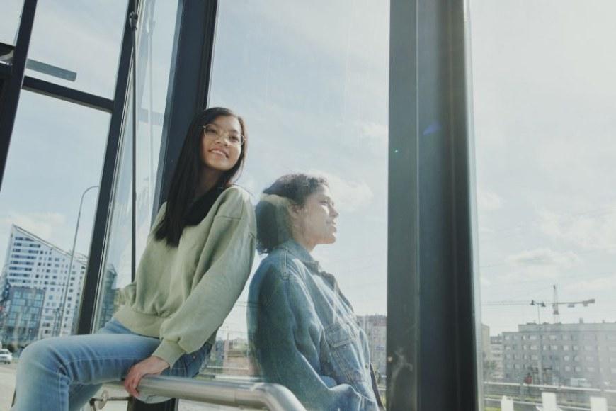 Kaksi nuorta naisopiskelijaa ison ikkunan äärellä kaupunkiympäristössä.