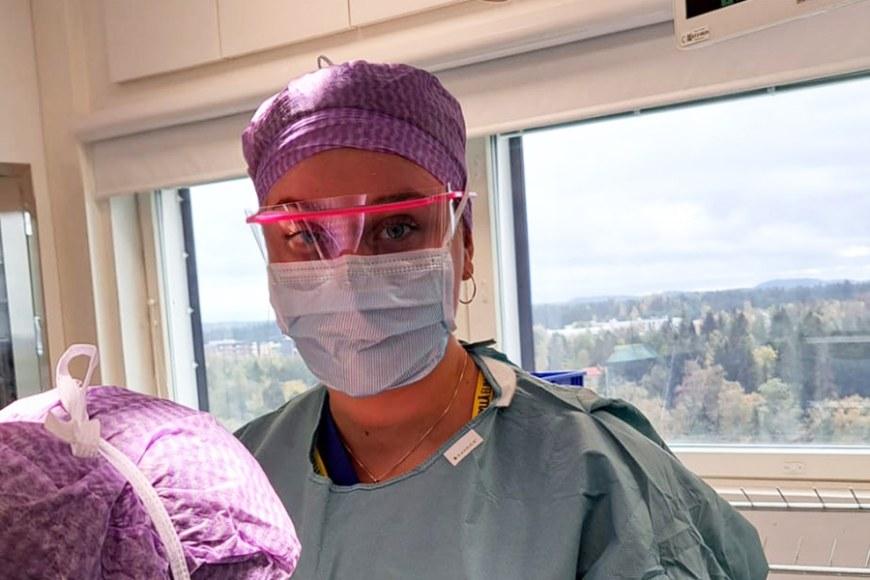 Sairaanhoitajaopiskelija Siina Kuusela työskentelee sairaanhoitajan työasussa, suojalaseissa ja maskissa.