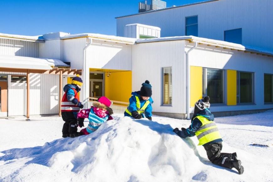 Lapsia leikkimässä pienen lumikasan päällä rakennuksen edessä.