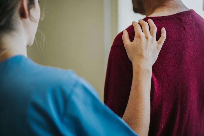 Naispuolinen sairaanhoitaja pitää kättään miespuolisen henkilön olkapäällä.