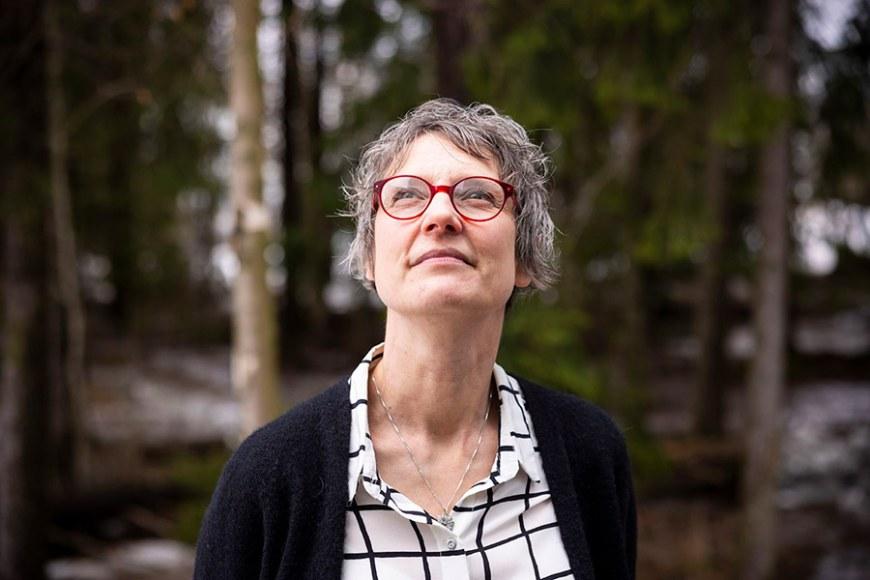 Katri Lindfors seisoo metsämaisemassa ja katsoo yläviistoon.
