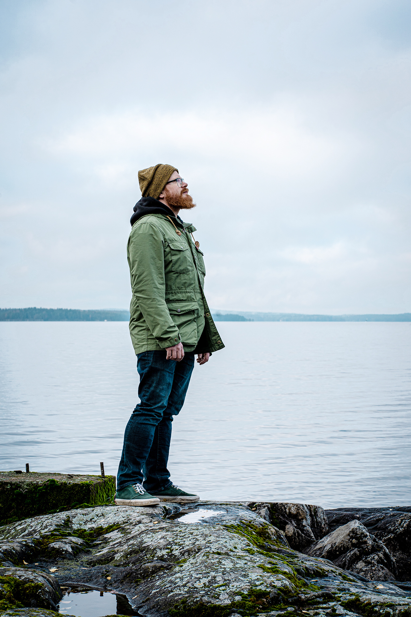 Parrakas henkilö seisoo kallion päällä järven rannassa katsoen yläviistoon