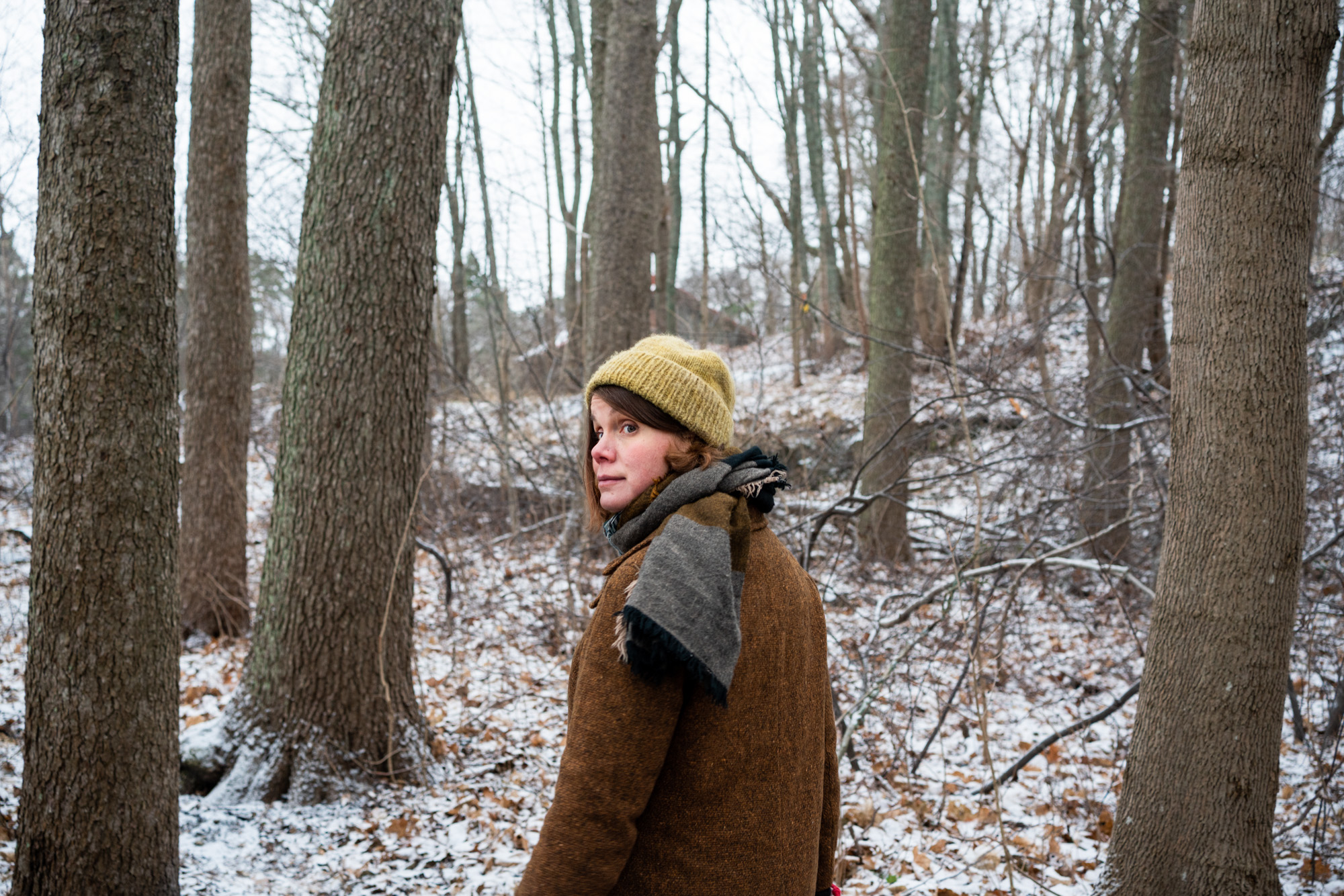 Naisoletettu kurkkaa olkansa yli kohti kameraa lumisessa metsässä.
