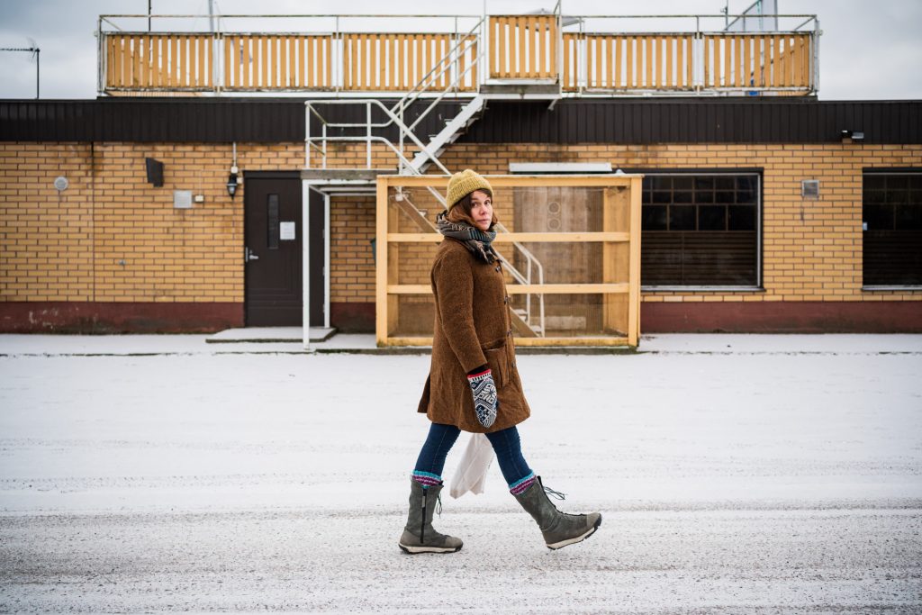 Naisoletettu kävelee lumisella tiellä, katse kohti kameraa.