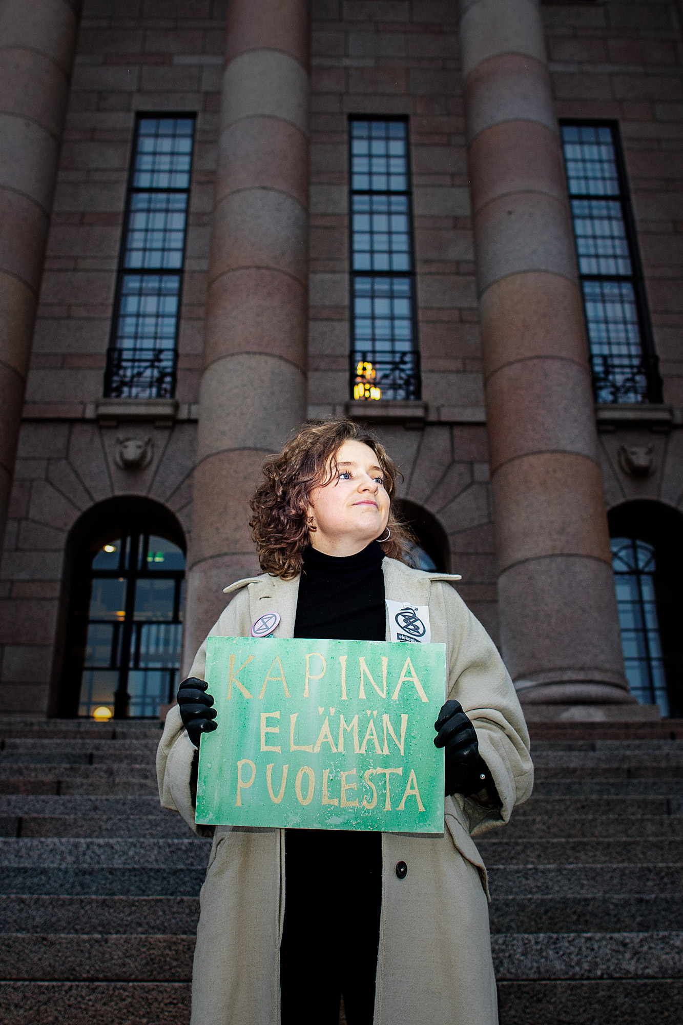 Nainen seisoo eduskuntatalon portailla Helsingissä, kädessään mielenosoitus kultti.