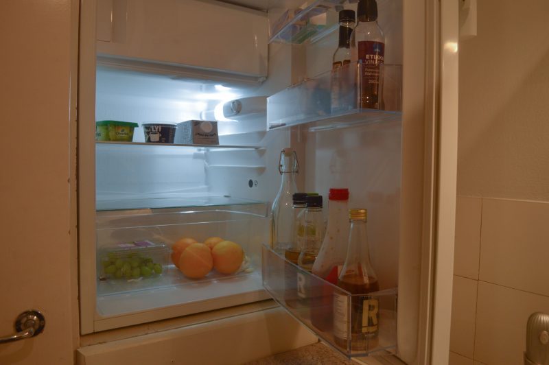 Kuvassa on auki oleva jääkaappi. Jääkaapissa on muun muassa appelsiineja, etikkaa ja kauramaitoa.