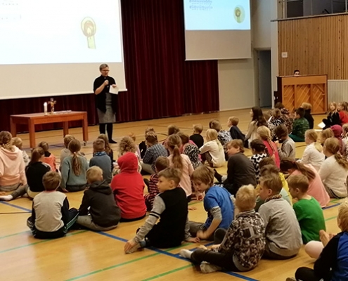 Kuvassa on alakoulun oppilaita salin lattialla istuen seuraamassa adventtihartauden ohjelmaa.