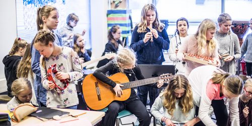 Kuvassa on kahdeksan alakoulun musiikkiluokan oppilasta soittamassa eri soittimia, kitaraa, nokkahuolua, ksylofonia ja rumpuja.
