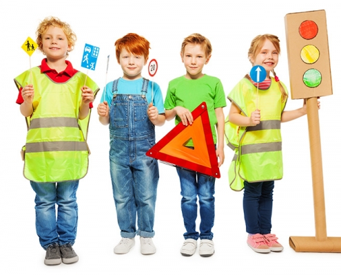 Kuvassa on poseeraamassa neljä iloista pikkulasta heijastinliivien ja liikennemerkkien kanssa.