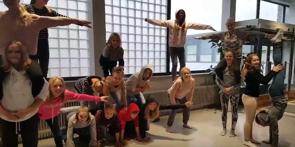 Kuvassa parikymmentä oppilasta on koulun aulassa erilaisissa akrobaattisissa asennoissa.