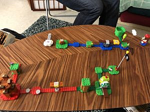 A LEGO course is on a table. Course starts with a water section, then moves to lava area and ends in a grassy area.