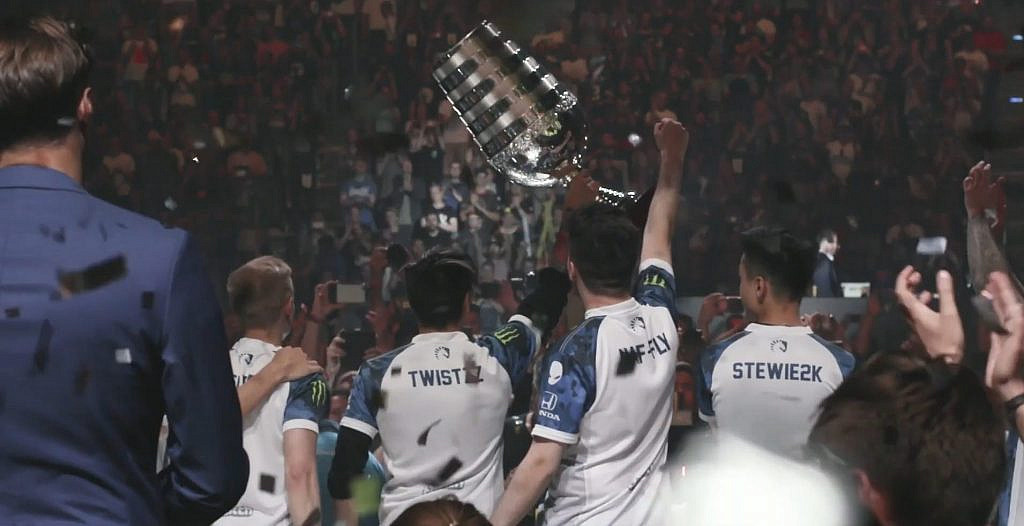 E-urheilijat nostavat pokaalin ilmaan yleisön edessä.