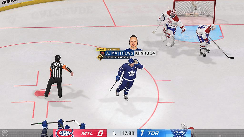 Sinipaitainen jääkiekkoilija tuulettaa tekemäänsä maalia vastustajien katsoessa vierestä.