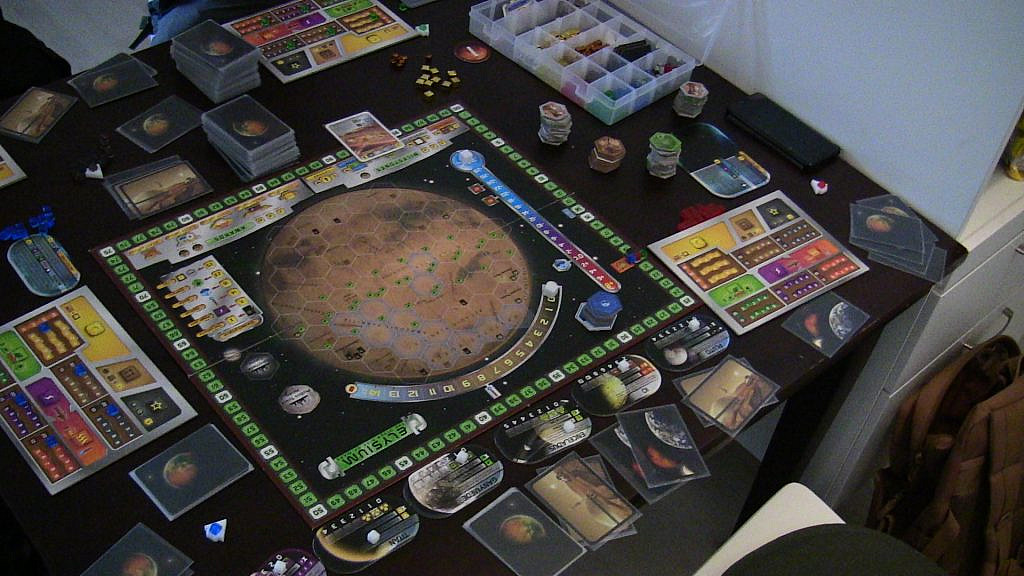 A lot of different cards and game pieces surrounding a large map of the planet Mars on the table.