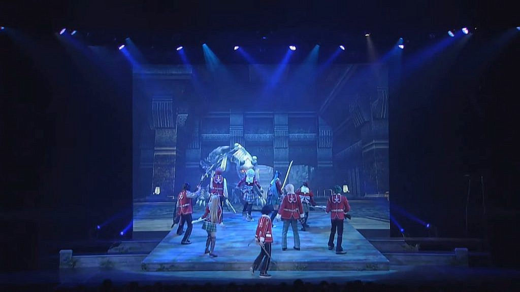 Group of students (actors) in the middle of a stage with a computer generated animation of a monster in the background center 