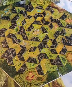 A hexagon game board with mountain landscape, made of multiple smaller hexagon pieces, black geometrical shapes on top of the hexagon pieces