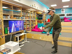A man wearing a VR headset playing Beat Sabre in a colourful room with a TV.