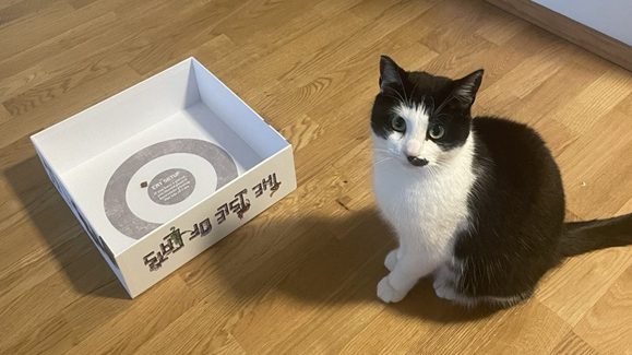 A board game box lid with text and a cat that's black and white.