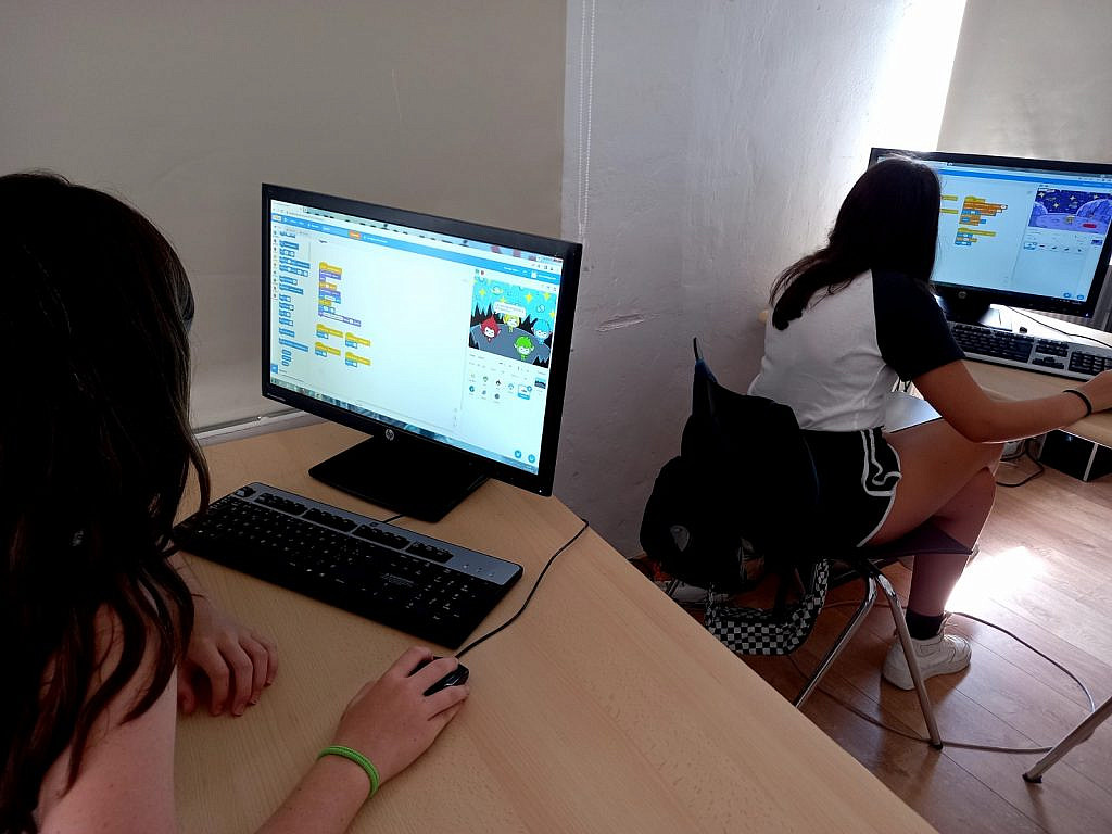 Two girls working on separate computers on making games in scratch