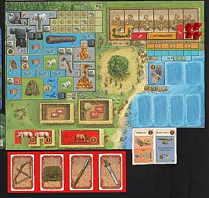 Village with colorful game tiles and characters placed, barn areas at the bottom, a large tree in the middle and a banquet table to the top right, shore has a boat, playing cards below village picture