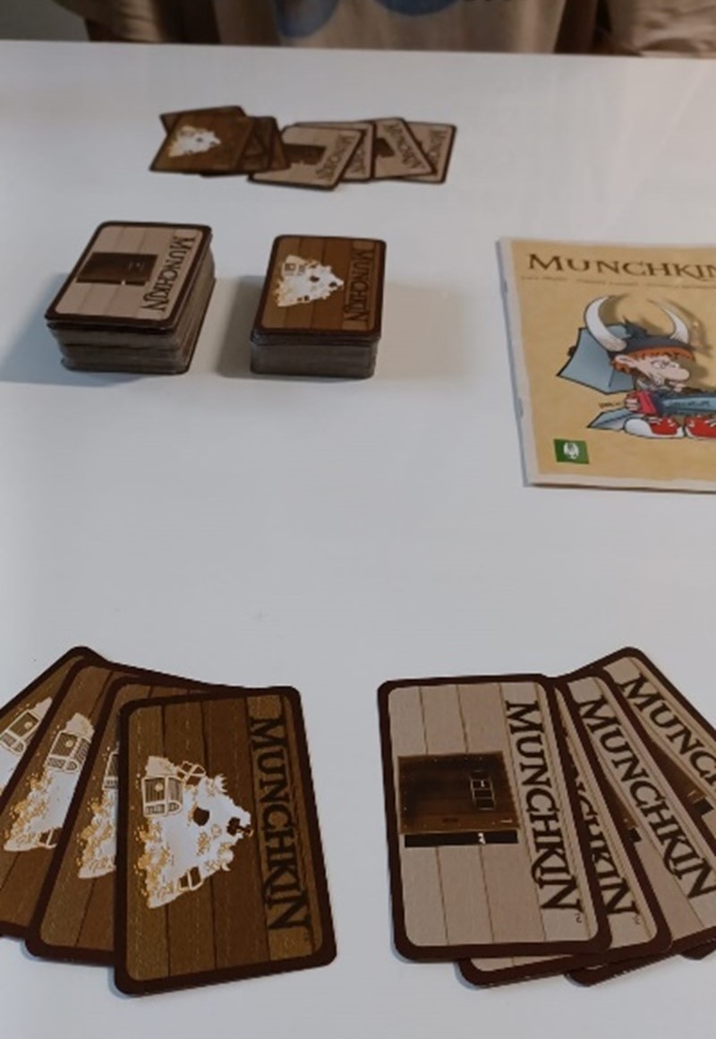 On the table, there is a rule sheet and two different Munchkin card decks from which players have drawn eight cards.