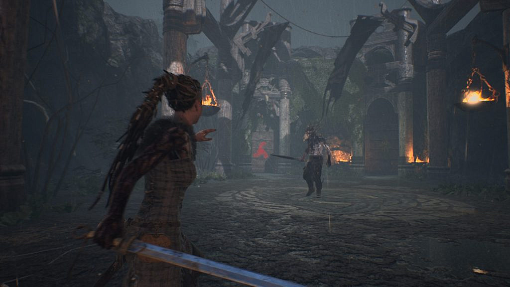 Woman holding a sword while facing animal skull -headed man in an arena like environment.