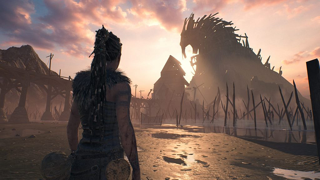 Woman at shore looking at mountain-like wood structure. 
