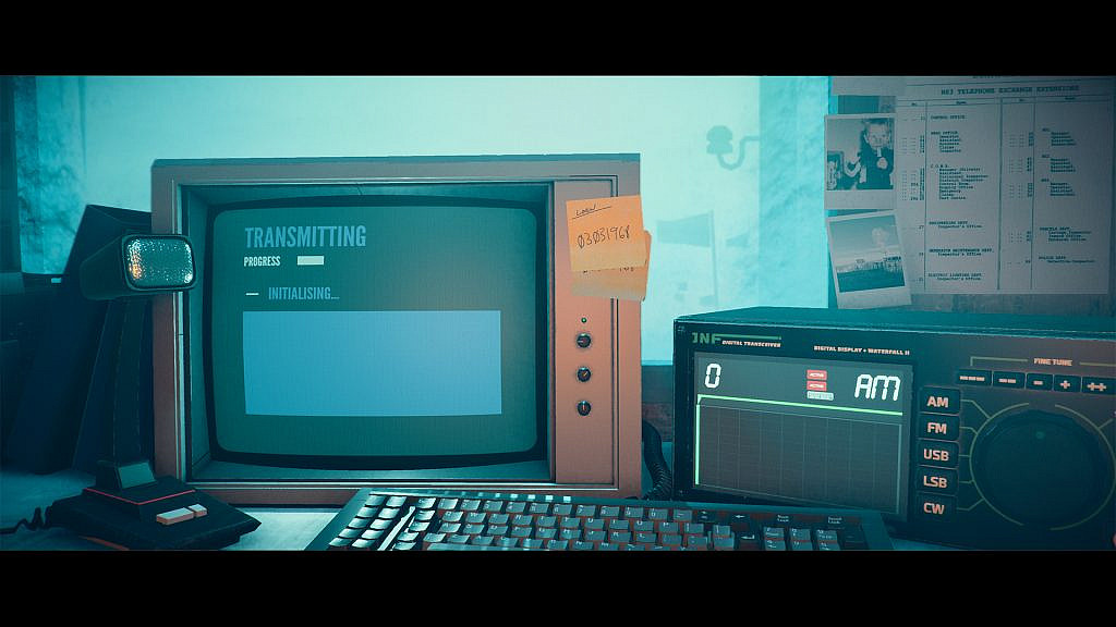An old computer and a radio on a desk. There is a post-it note with code on the computer. Behind the desk there are papers and photos attached on the wall behind the desk