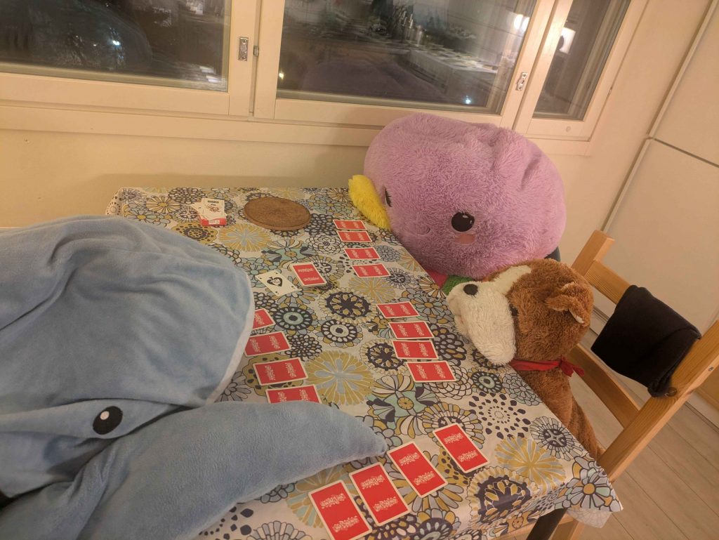 A table with a stuffed shark, octopus thing, dog. Cards are laid in front of them - four face down. They're playing cambio <3