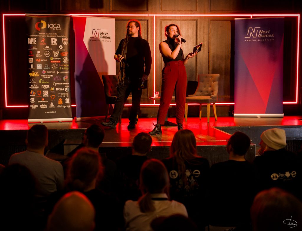 Two people standing on a stage with microphones, there is a crowd sitting down below them.