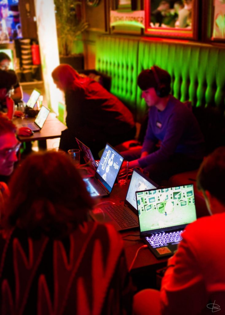 Multiple people sitting around a table in a moody bar in front of laptops 
