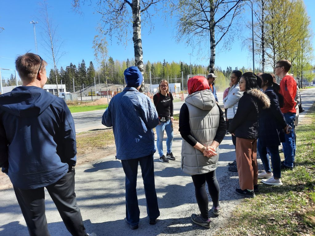 The group of people standing on a walkway and listening Aino to describe the method.