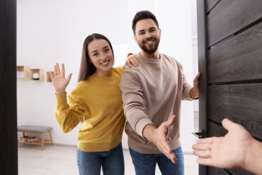 Happy couple welcoming their guest near door. Invitation to come indoors